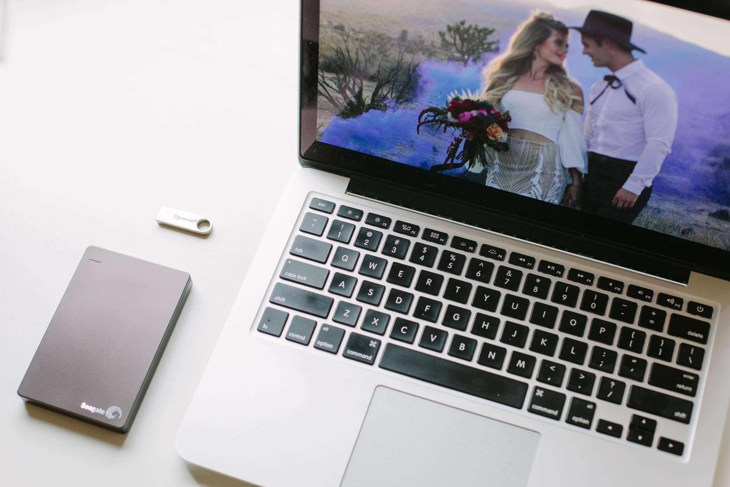 Photo of a wedding video on a laptop with an external hard drive and flash drive.